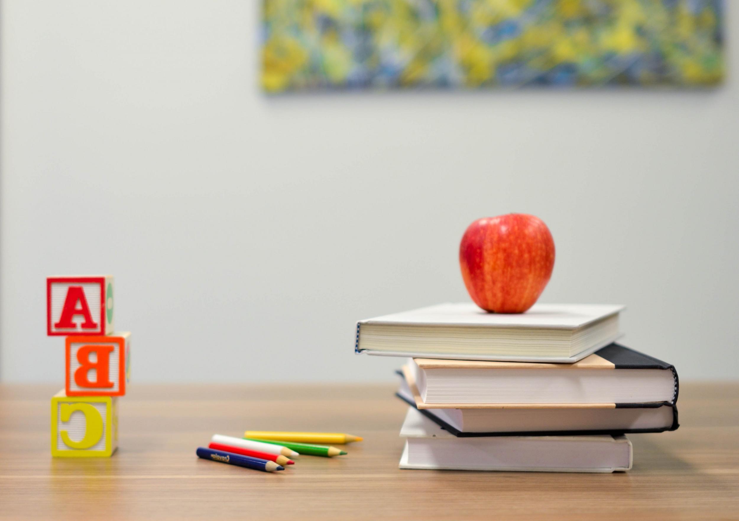 stack of three books on a desk with a red apple on top and a, b, c block cubes to the side